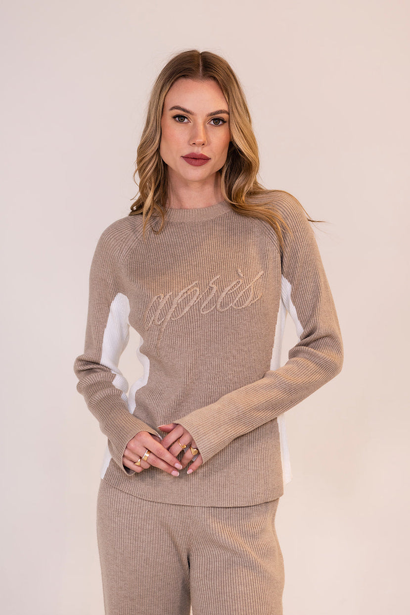 Woman wearing a beige ribbed knit sweater with 'après' text embroidered on the front.