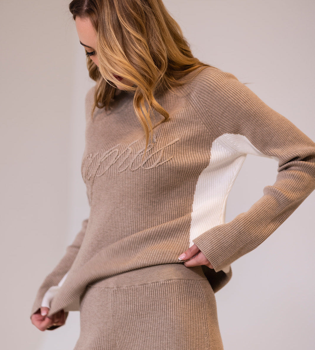 Woman wearing a beige ribbed knit apres actif sweater and pants with &#39;Apres&#39; embroidered across chest